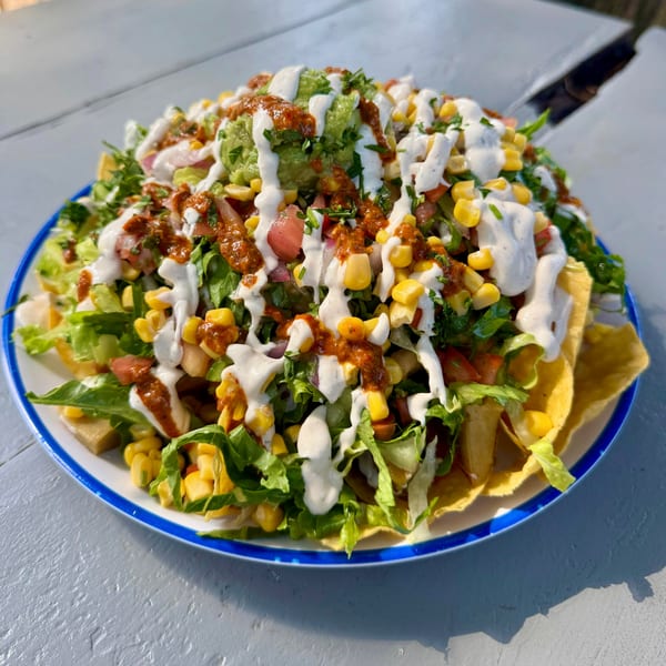 A large plate of nachos topped with lettuce, corn, salsa, guacamole, and white sauce.
