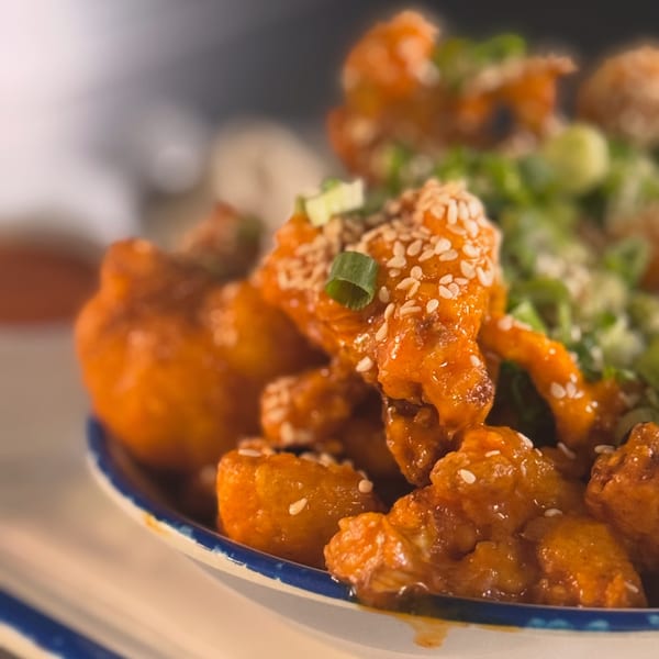 Close-up of orange-glazed fried chicken bites topped with sesame seeds and chopped green onions.