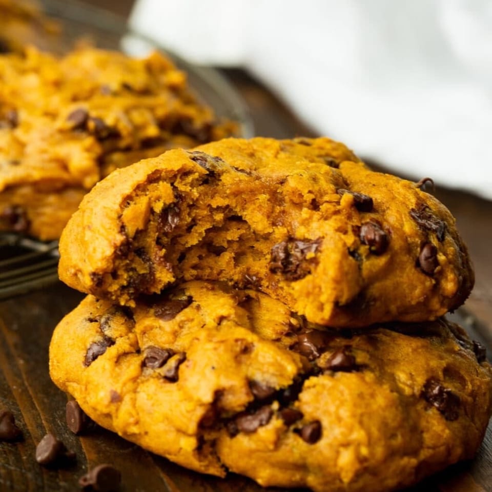 Stack of golden chocolate chip cookies on a dark wooden surface.