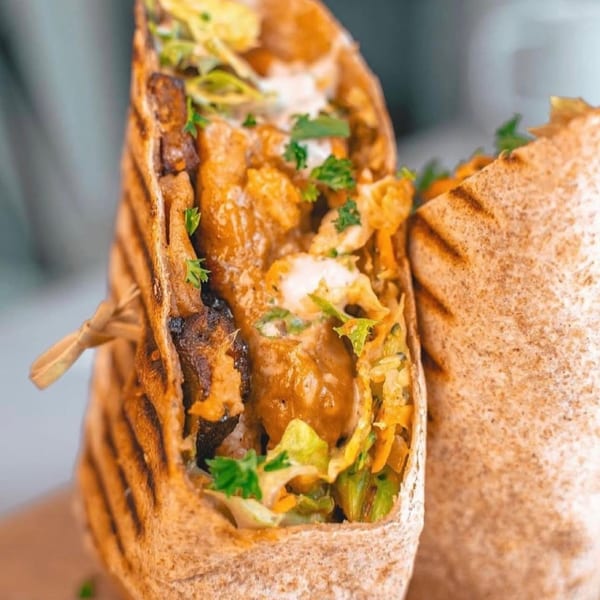 Close-up of a grilled chicken wrap filled with lettuce, sauce, and cilantro, held by a wooden pick.