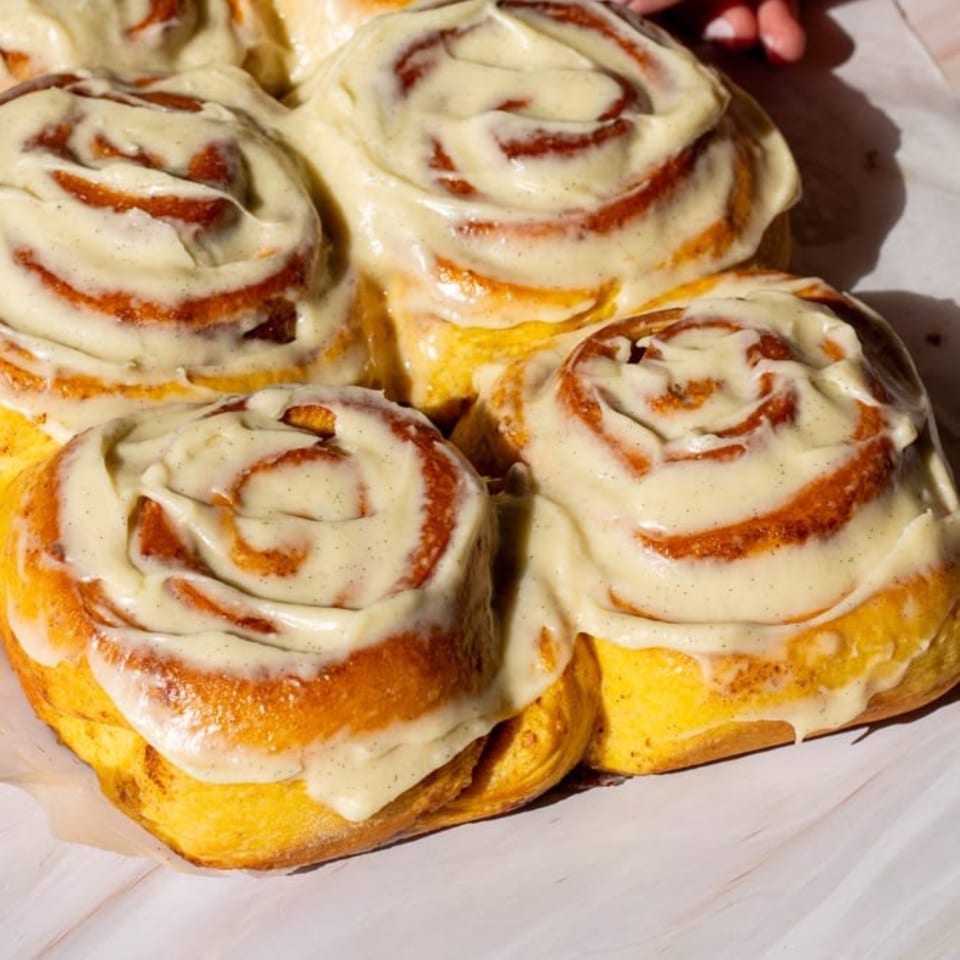 Golden cinnamon rolls topped with creamy icing arranged on a baking tray.