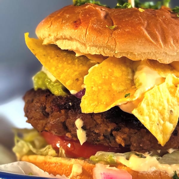 Close-up of a burger with a thick patty, guacamole, sour cream, and tortilla chips.
