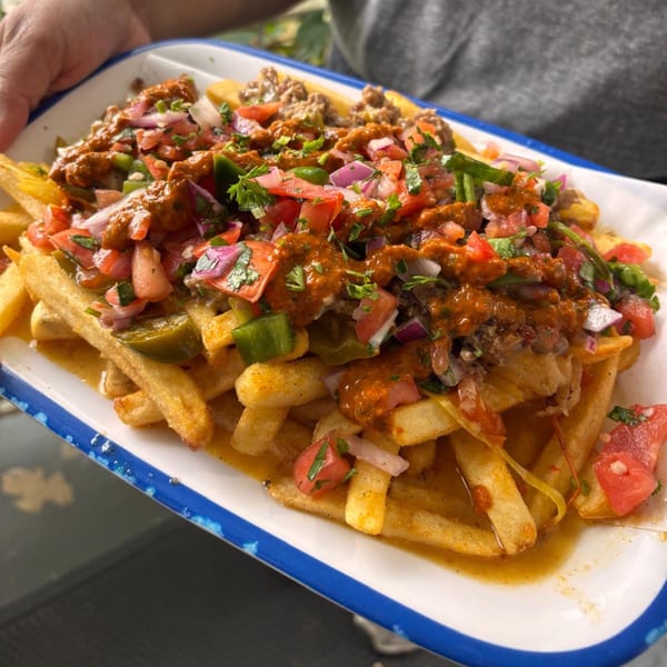Close-up of chili cheese fries topped with pico de gallo, jalapeños, and cilantro.