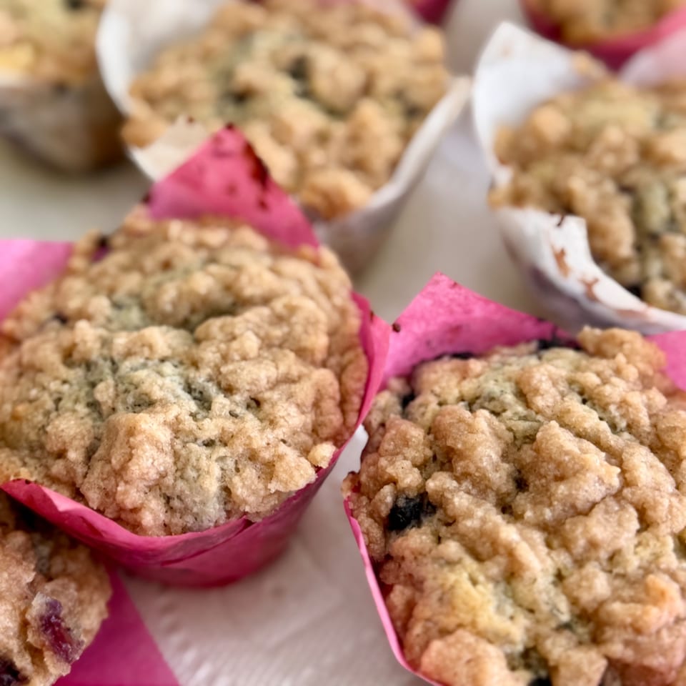 Golden-brown crumb muffins arranged in bright pink paper cups on a serving table.