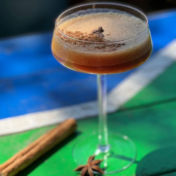 Espresso martini with coffee beans and cinnamon stick on a blue and green striped surface.