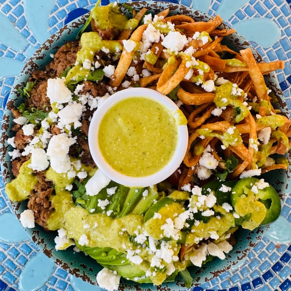 A vibrant Mexican salad bowl with ground meat, tortilla strips, avocado, and green dressing.