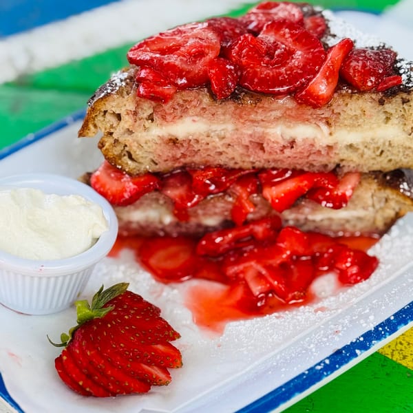 Strawberry stuffed French toast with whipped cream and a sliced strawberry on a white plate.