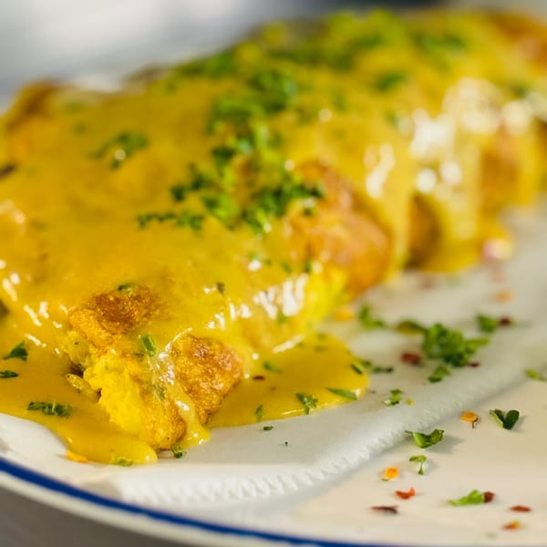 Close-up of a golden-brown dish covered in a rich yellow sauce and sprinkled with green herbs.