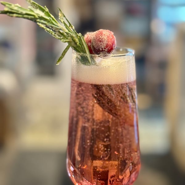Sparkling pink cocktail in a champagne flute, garnished with sugared cranberries and rosemary.