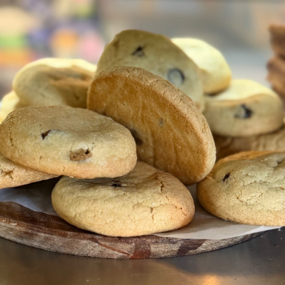 Assorted golden-brown cookies with chocolate chips stacked on a rustic serving tray.